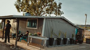 En lille, etetagers bygning med metalfacade, en veranda med bænk og plantekasser.
