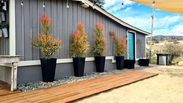 A building with a grey exterior, a wooden deck, and potted plants.