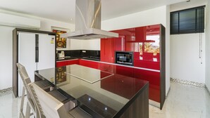 A modern kitchen with a central island, stainless steel appliances, and red cabinetry. - 3 Bedroom Sea View Villa Mattana 2 SDV162 - Chaweng Noi - By Samui Dream Villas (Koh Samui)