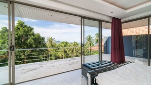 A modern bedroom with a large sliding glass door leading to a balcony with a view of palm trees and a red-roofed building. - 3 Bedroom Sea View Villa Mattana 2 SDV162 - Chaweng Noi - By Samui Dream Villas (Koh Samui)