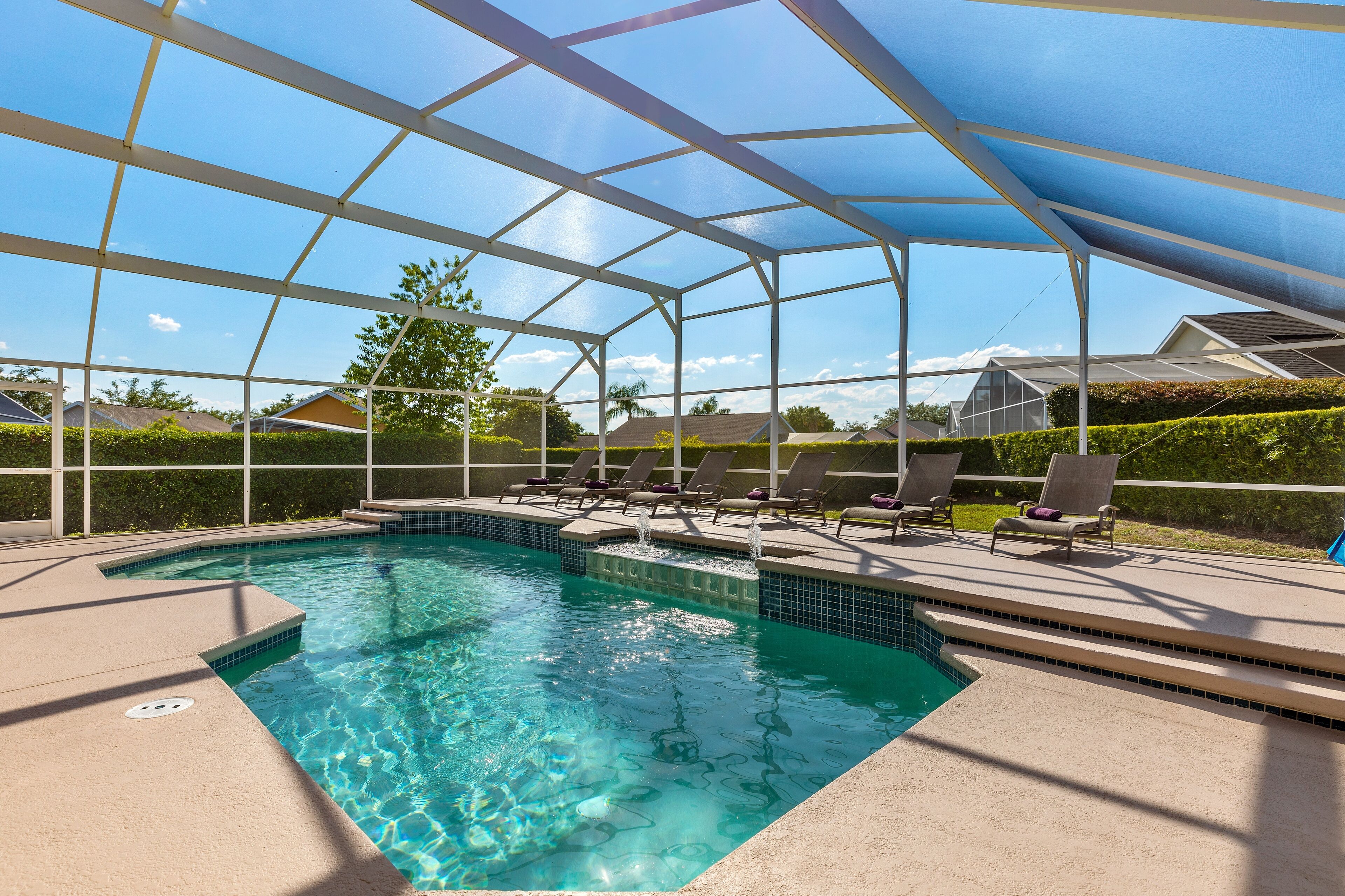A pool area with a glass enclosure, clear blue water, and several lounge chairs.