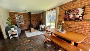 A cozy living room with a brick fireplace, a dining table, and a sofa. - Mogendoura Farm 3 COTTAGES MAX 12 ADULTS but 18 people including children (Moruya)