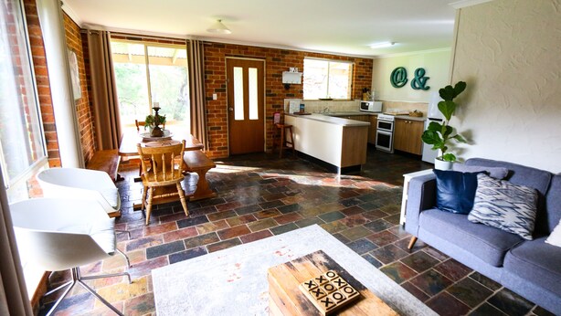 A spacious living area with a sofa, a dining table, and a kitchen in the background. - Mogendoura Farm 3 COTTAGES MAX 12 ADULTS but 18 people including children (Moruya)