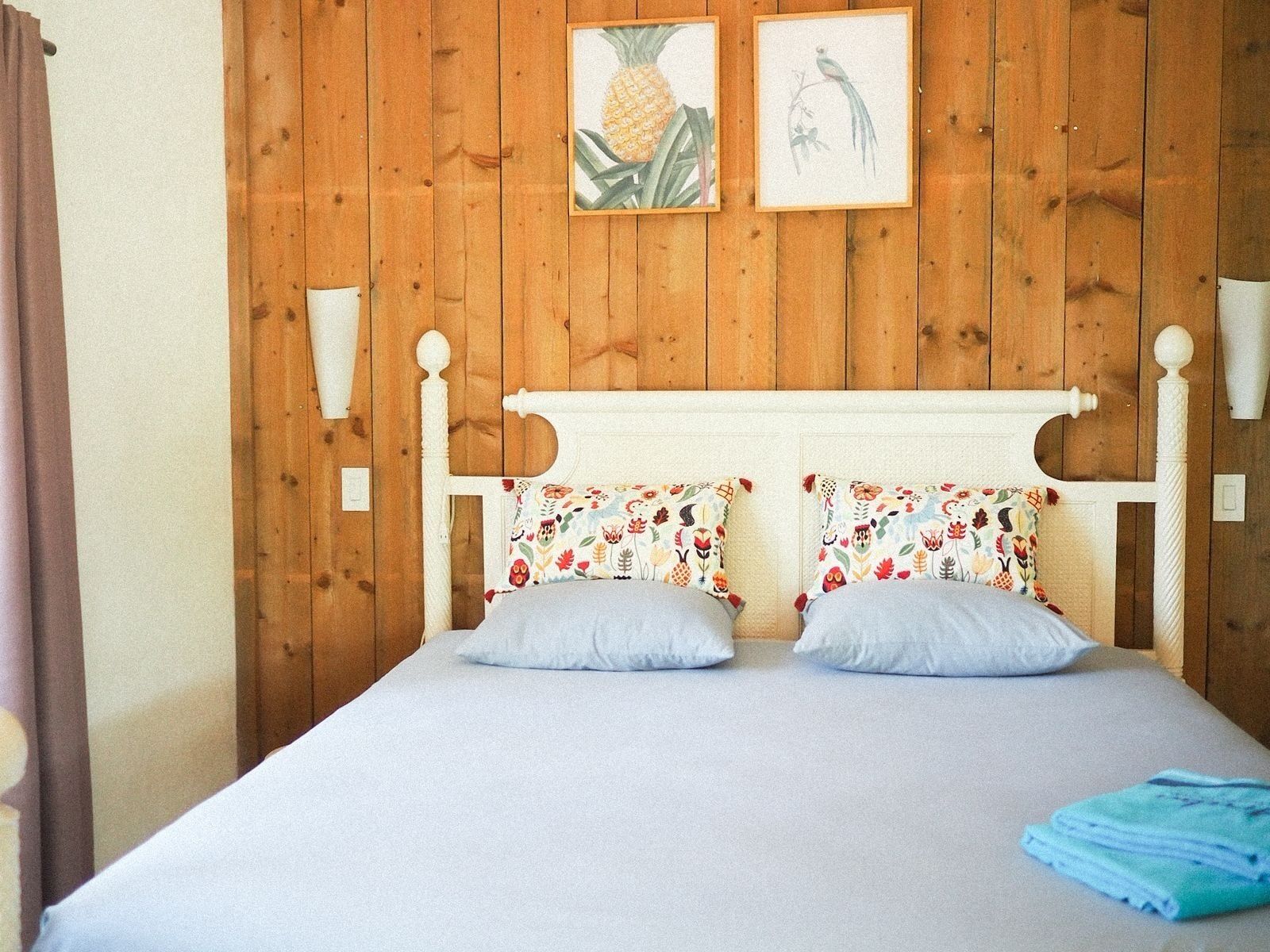 Een bed met een houten hoofdbord, twee sierlijke kussens en een blauwe deken.