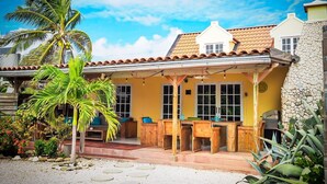 Una casa amarilla con techo de tejas, porche de madera y pared de piedra.