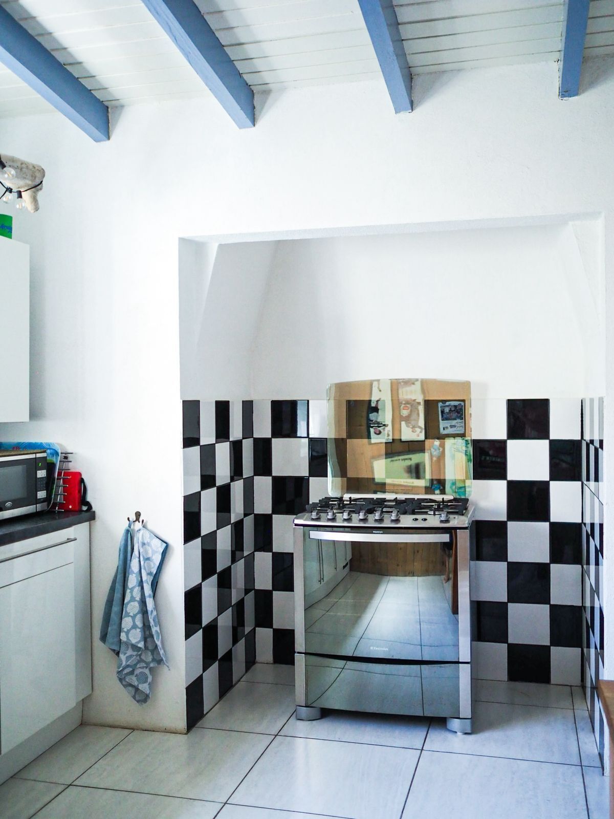 Een kleine keuken met een gasfornuis, een magnetron en een spoelbak. De muren zijn betegeld met een zwart-wit ruitpatroon.