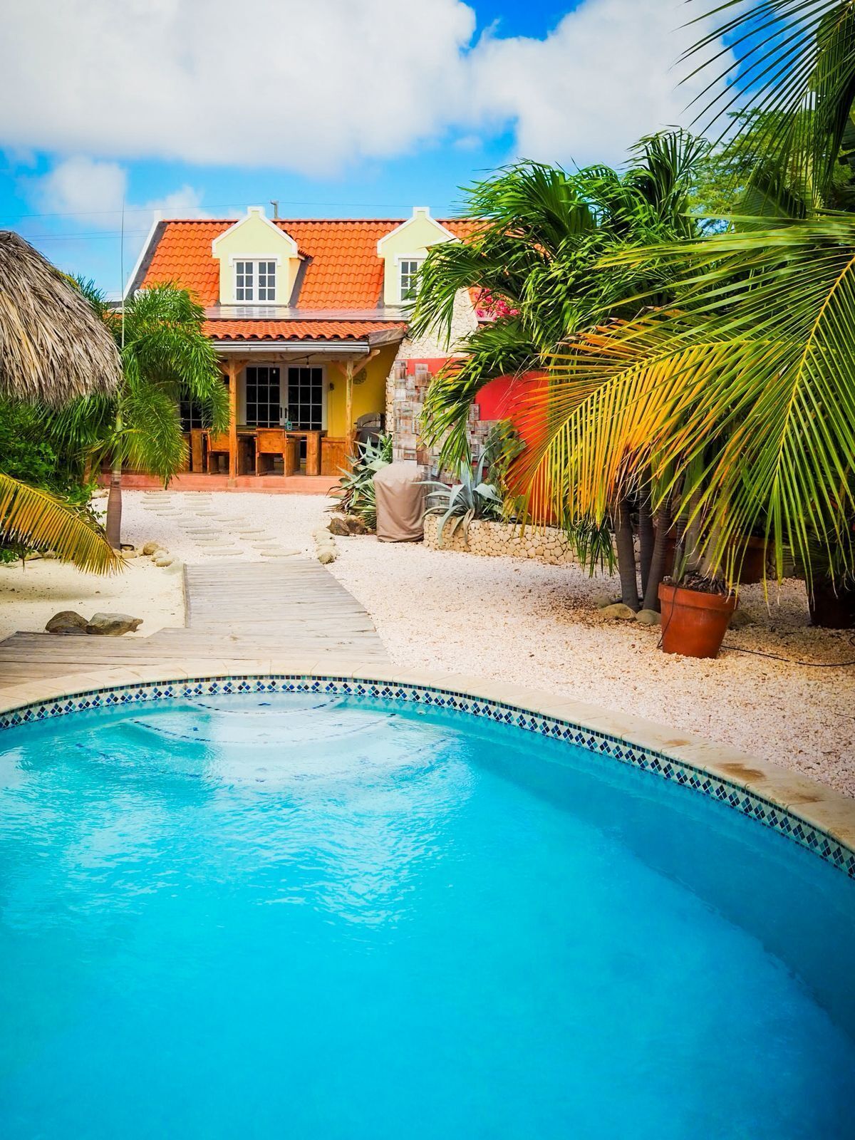 A swimming pool with a tiled edge, surrounded by a sandy area and palm trees.