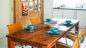 Comedor con paneles de madera, una mesa de madera, sillas naranja y una lámpara colgante.
