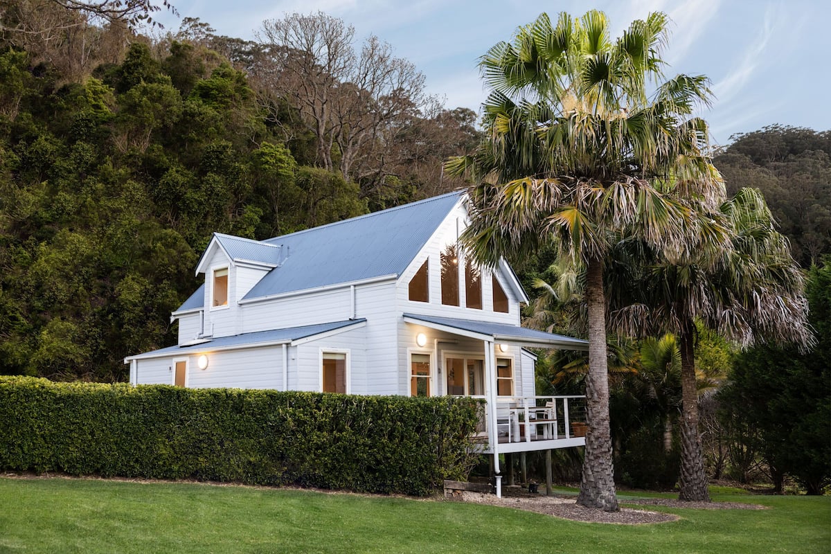 A white house with a blue roof, surrounded by lush greenery and a palm tree.