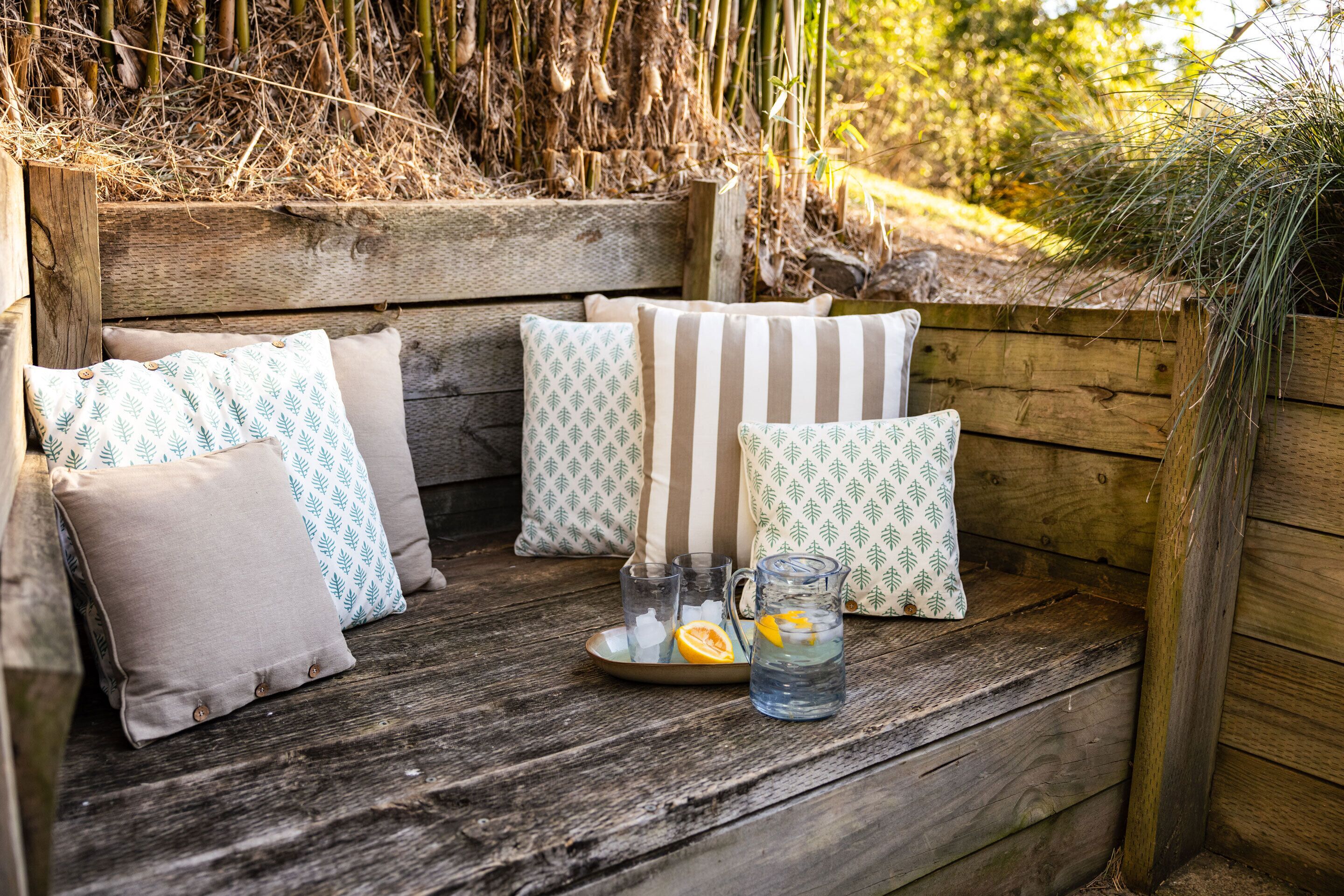 A wooden bench with cushions, a pitcher of water with lemon slices, and a tray with ice cubes.