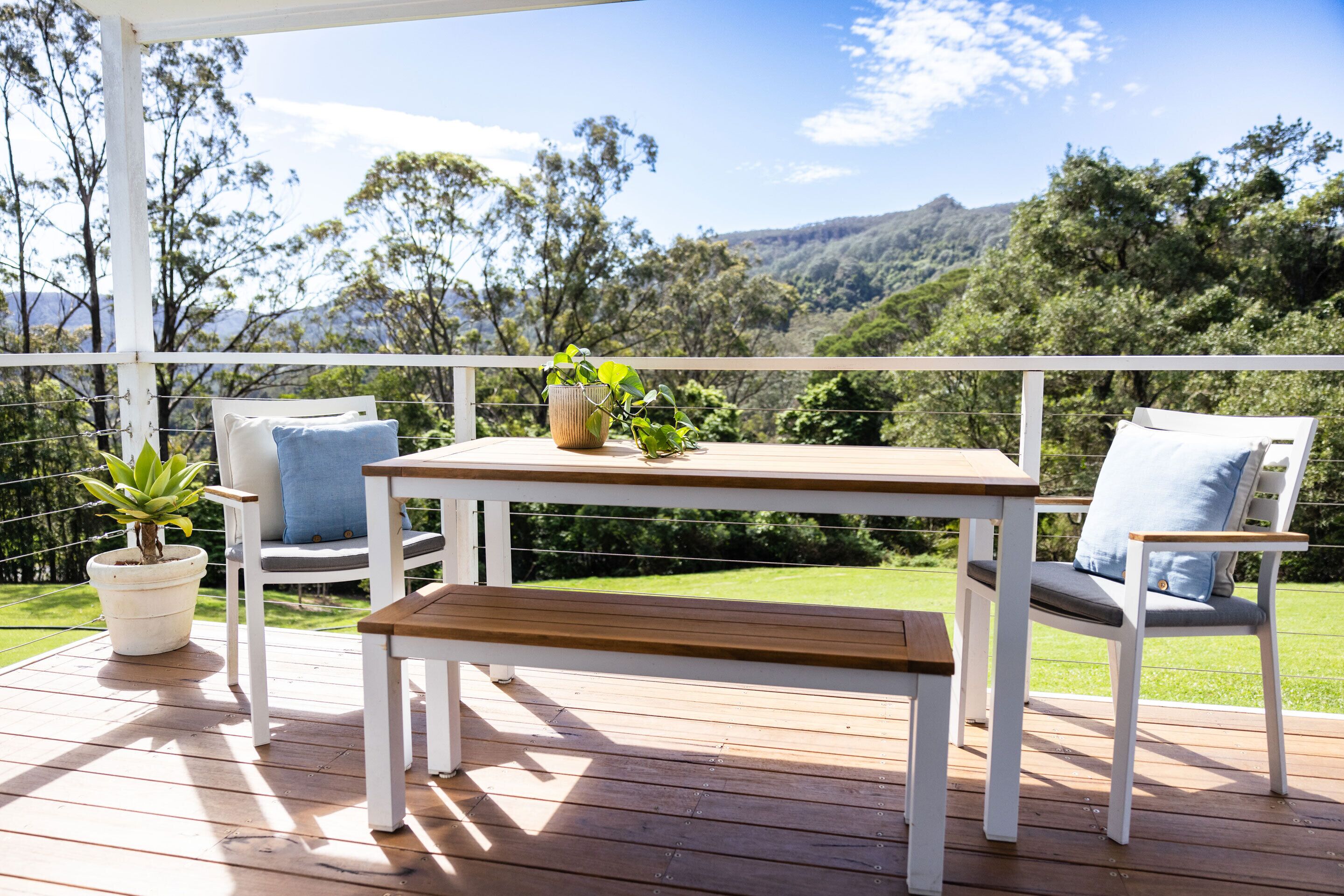 A wooden deck with a table and two chairs, a bench, and a potted plant.