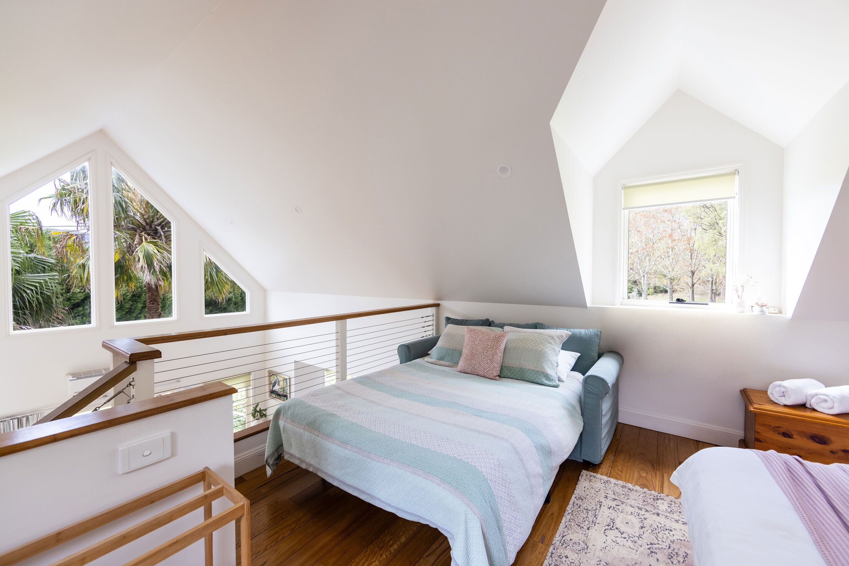 A bedroom with a bed, a window, a wooden staircase, and a view of trees.