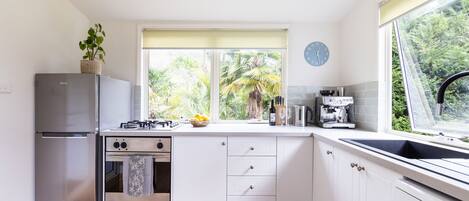 Una cocina moderna con armarios blancos, un refrigerador de acero inoxidable, una estufa a gas y una ventana con vistas a la vegetación.