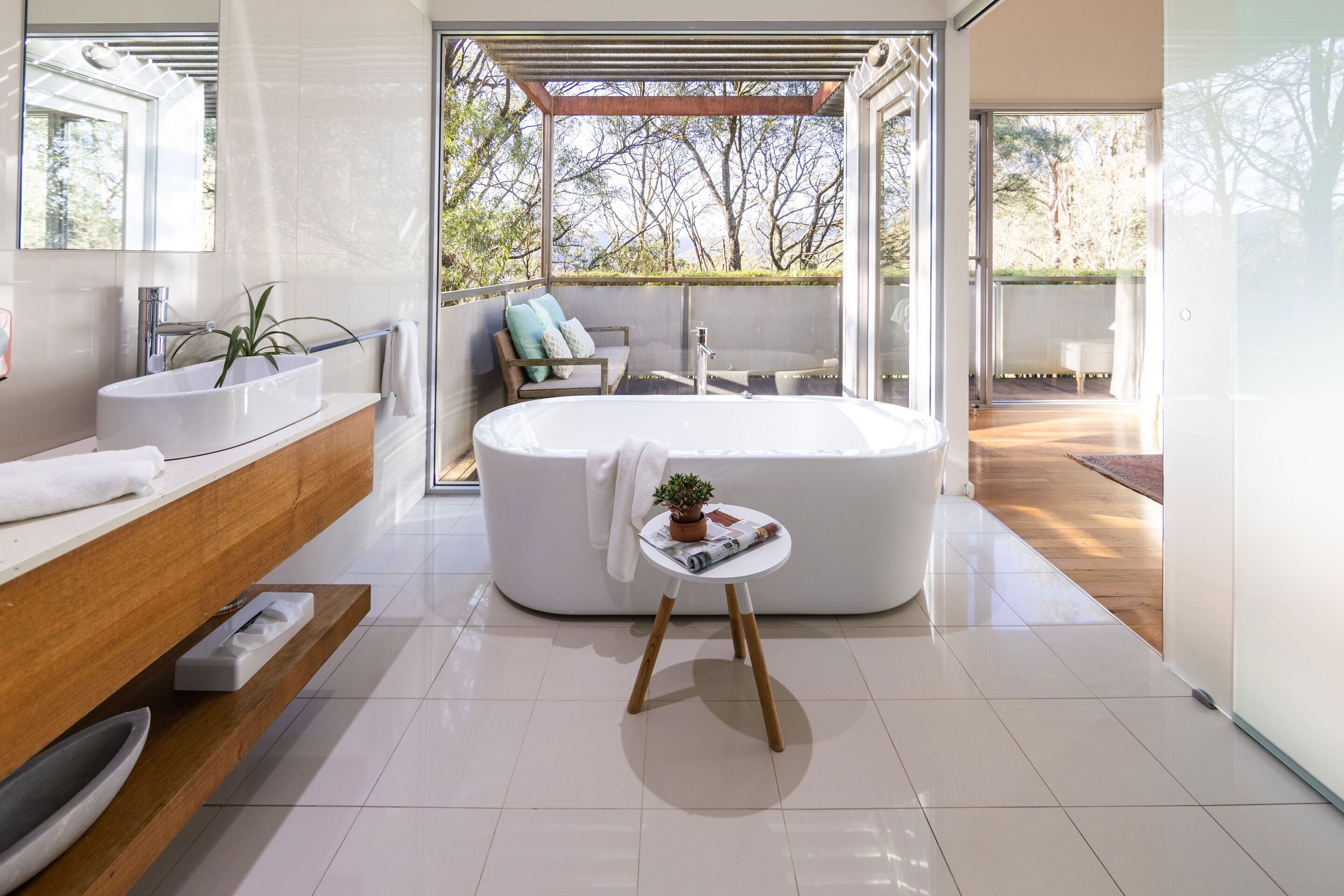 A modern bathroom with a freestanding bathtub, a wooden vanity, and a small table with a plant.