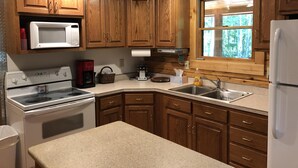 A kitchen with wooden cabinets, a microwave, a stove, a sink, and a refrigerator. - New Log Cabin On 3 Wooded Acres, Outdoor Shower, Lake Michigan,  Air-Conditioned (Mears)