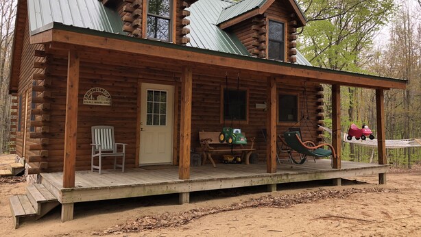A log cabin with a porch, a wooden chair, a table, and a swing. - New Log Cabin On 3 Wooded Acres, Outdoor Shower, Lake Michigan,  Air-Conditioned (Mears)