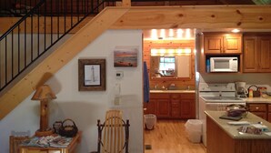 A wooden interior with a staircase, a kitchen area with wooden cabinets, a microwave, and a dining area with a table and chairs. - New Log Cabin On 3 Wooded Acres, Outdoor Shower, Lake Michigan,  Air-Conditioned (Mears)