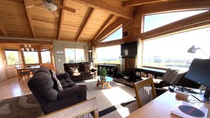 Ein gemütliches Wohnzimmer mit Kamin, Essbereich und großen Fenstern mit Blick ins Freie.