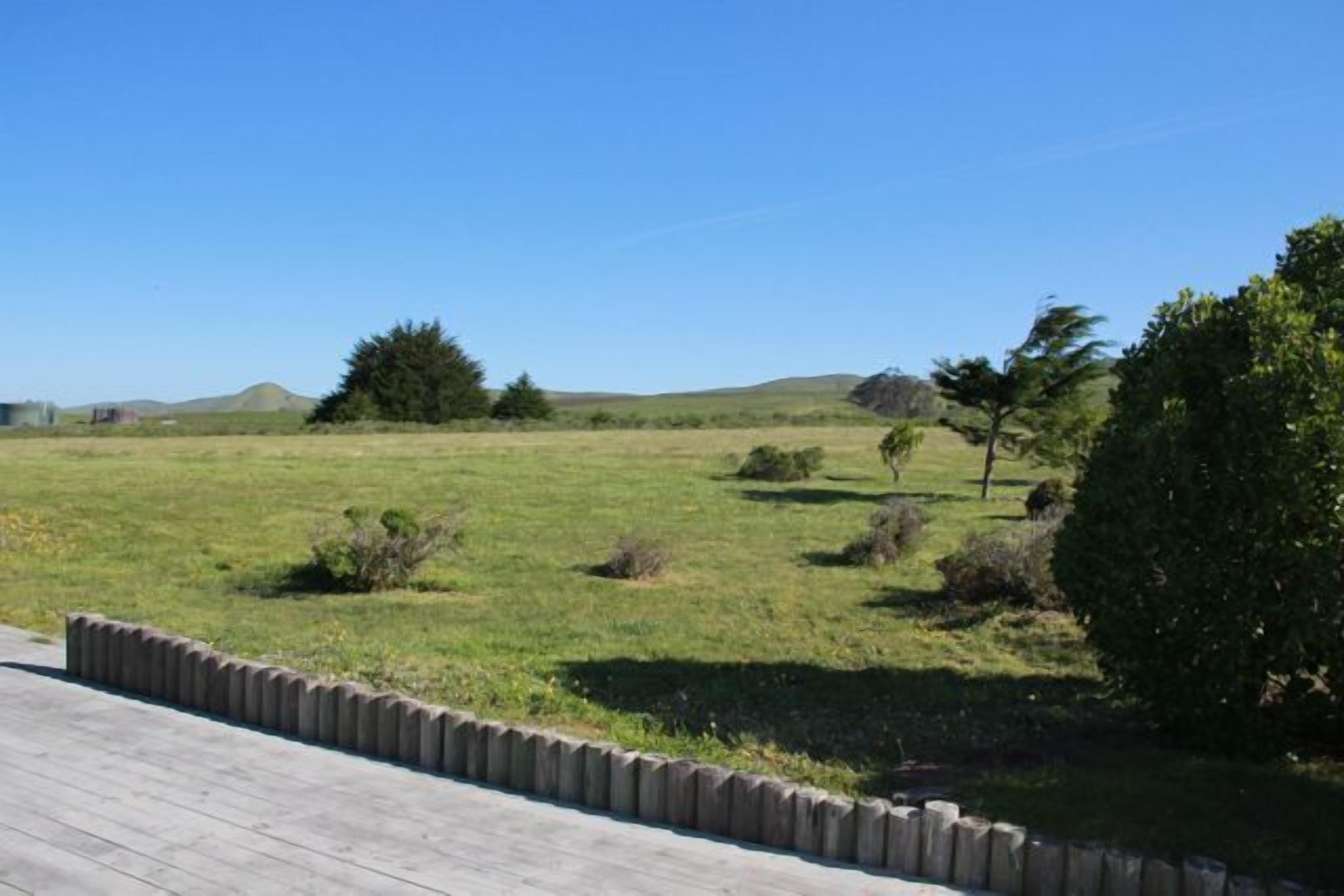 A grassy field with a wooden deck and a stone wall.