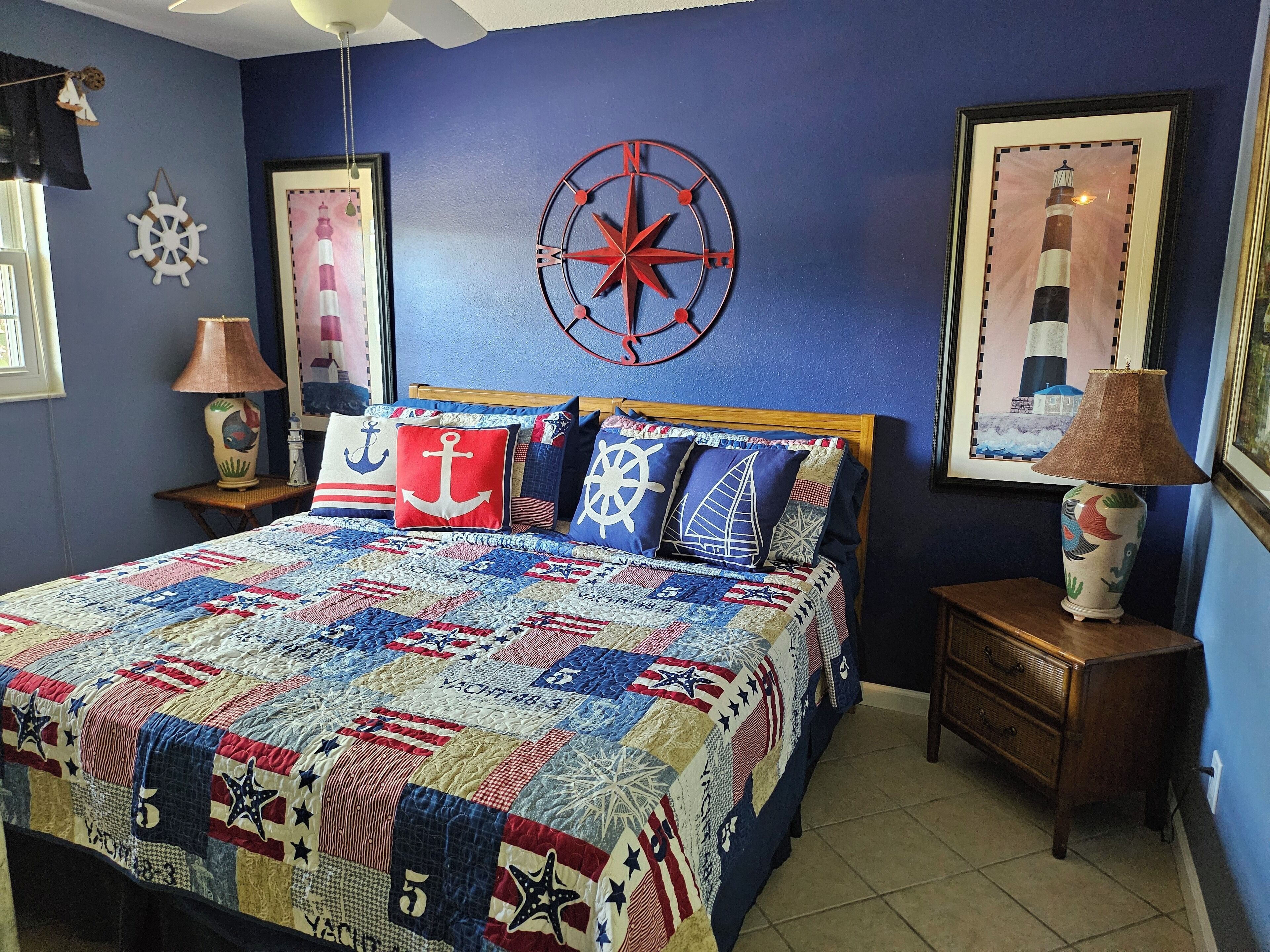 A bedroom with a nautical-themed bedspread, a compass wall decoration, and a lighthouse painting.