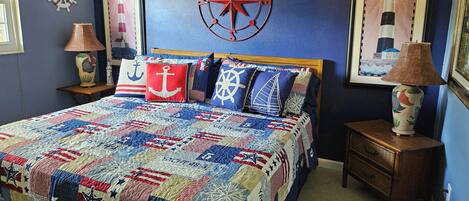A bedroom with a nautical-themed bedspread, a compass wall decoration, and a lighthouse painting.