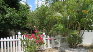 Un jardin avec une clôture en bois peinte en blanc, diverses plantes vertes et des fleurs roses.