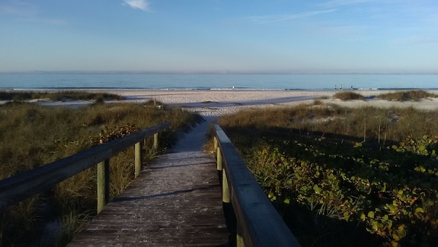 Une promenade en bois qui mène à une plage bordée de dunes, sous un ciel dégagé.