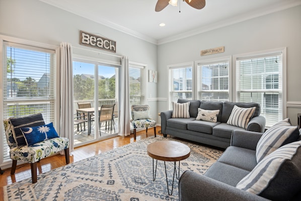 A spacious living room with a gray sofa, a patterned rug, and a view of the outdoors through large windows.