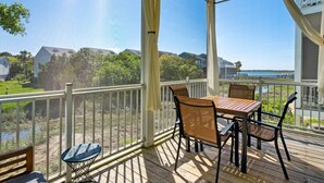 A covered outdoor area with a table and chairs, a bench, and a view of a body of water and greenery. - Water's Edge 103 - Bright 3BR/3BA Townhome - Pool - Fishing Dock (Folly Beach)