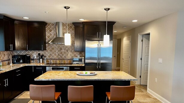 A modern kitchen with dark cabinets, a granite island, stainless steel appliances, and pendant lighting.