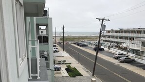 A view of a street with parked cars and a building with a balcony.