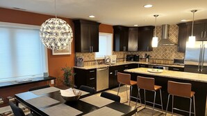 A modern kitchen with dark cabinets, a central island, and a dining area with a black table and chairs.