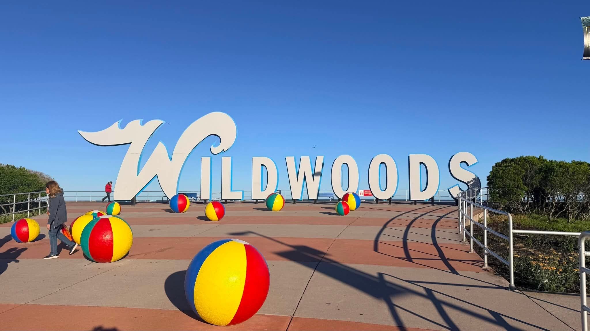 Un letrero grande al aire libre que dice 'WILDWOOODS' con coloridas pelotas de playa al frente.