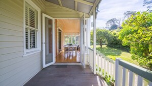 Eine überdachte Veranda mit Esstisch und Stühlen, eine Holzterrasse und Blick auf einen üppigen Garten.