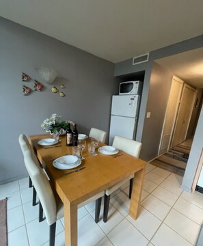 Un coin repas avec une table en bois dressée pour quatre personnes, des chaises blanches et un réfrigérateur blanc en arrière-plan.