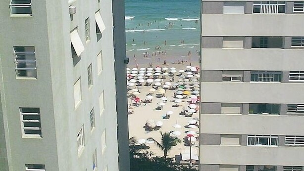 Un edificio de gran altura con varios balcones que dan a una playa con numerosas sombrillas.