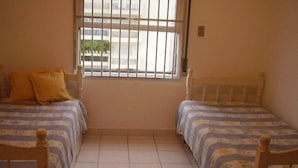 Una habitación con dos camas, una ventana con rejas y piso de baldosas.
