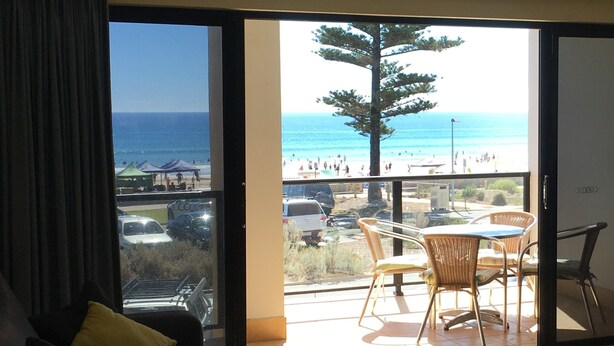 A living room with a large sliding glass door leading to a balcony with a view of the beach and ocean.