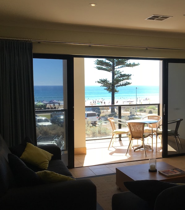 A living room with a large sliding glass door leading to a balcony with a view of the beach and ocean.