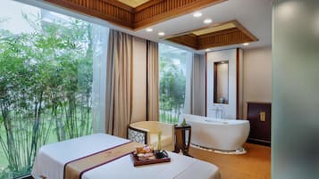 A hotel room with a large bed, a bathtub, and a view of greenery.