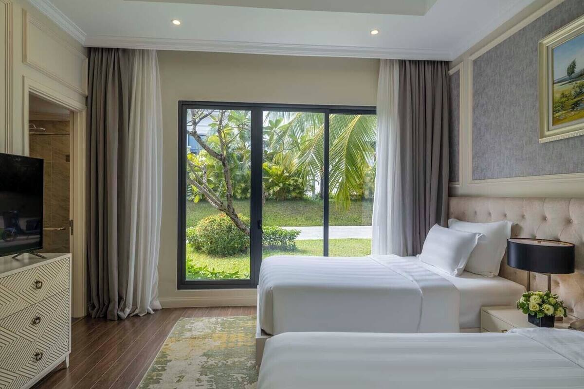 Een hotelkamer met twee bedden, een televisie, een groot raam met uitzicht op groen en een schilderij aan de muur.