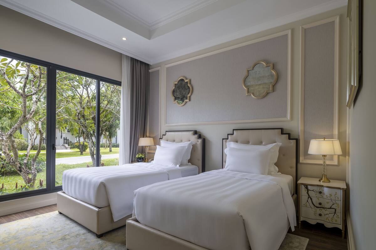 Een hotelkamer met twee bedden, een groot raam en uitzicht op groen.