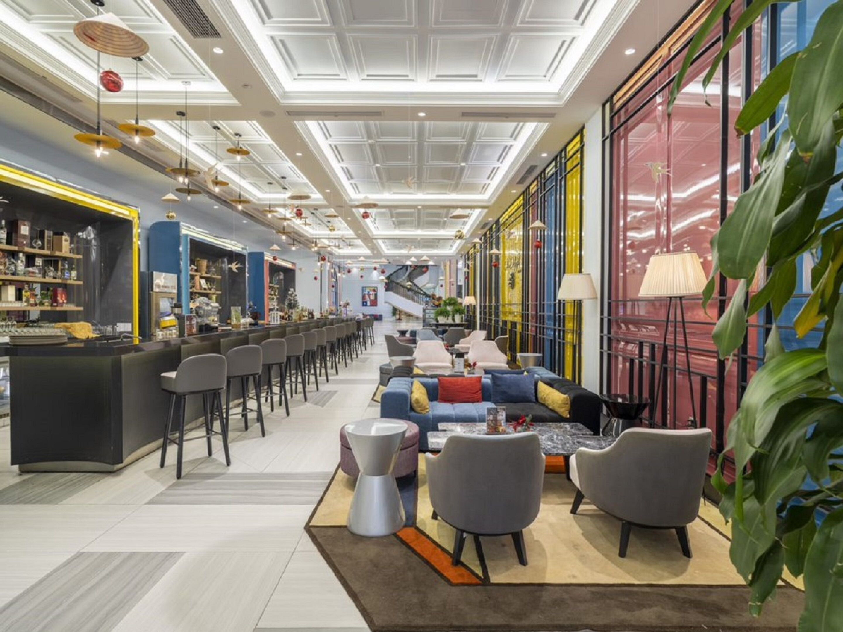 A modern hotel lobby with a bar area, seating, and a staircase leading to an upper floor.