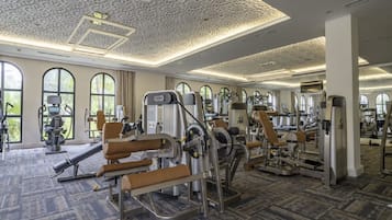 A gym with various exercise machines, large windows, and a patterned ceiling.