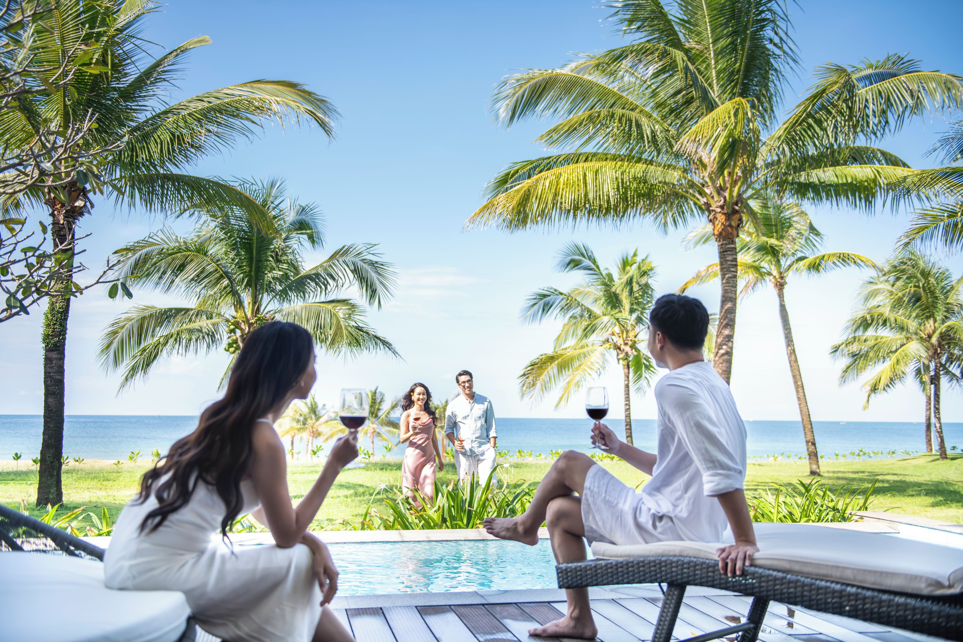 A poolside area with lounge chairs, a pool, and palm trees.