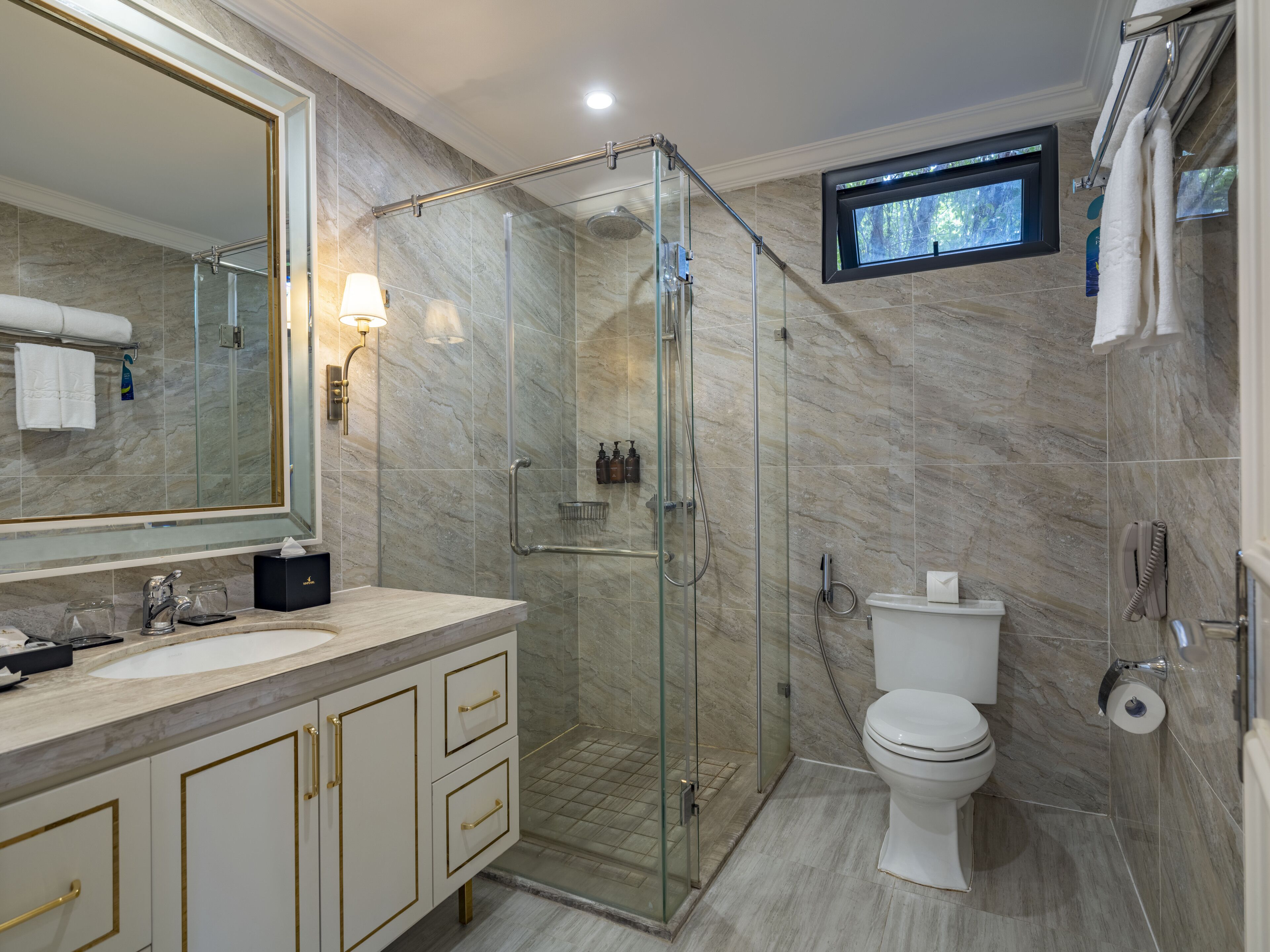 A modern bathroom with a glass-enclosed shower, a large mirror, a sink with a marble countertop, and a toilet.