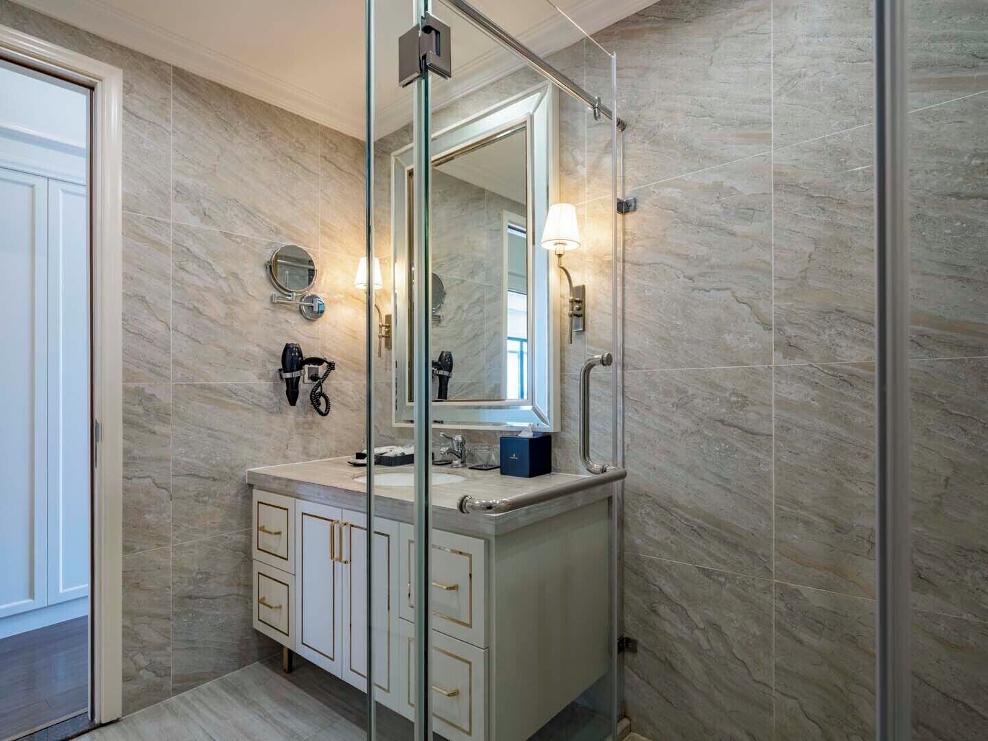 A modern bathroom with a marble wall, a large mirror, a hairdryer, and a towel rack.