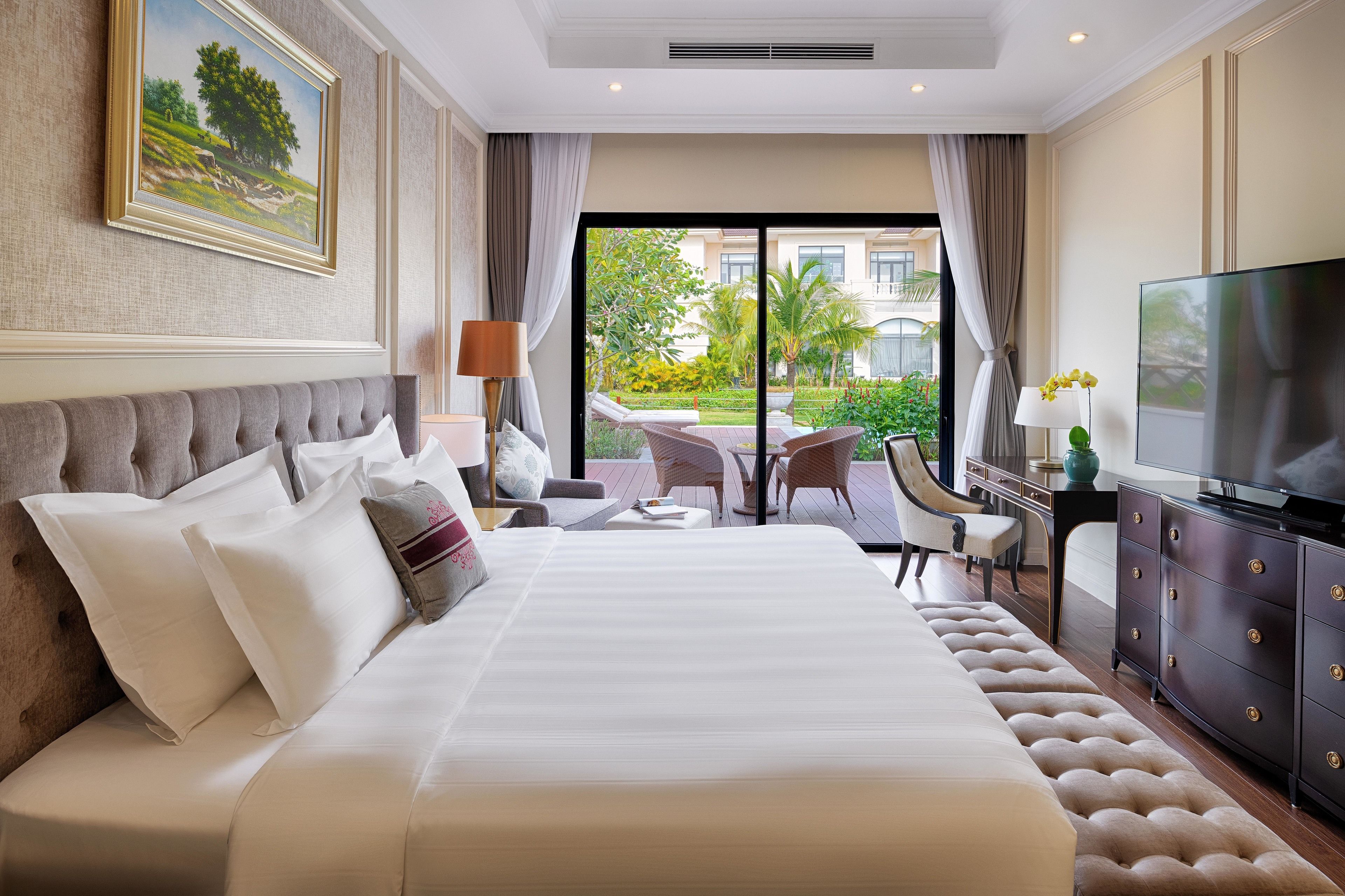 A hotel room with a large bed, a TV, a desk with a chair, and a view of the outdoors.