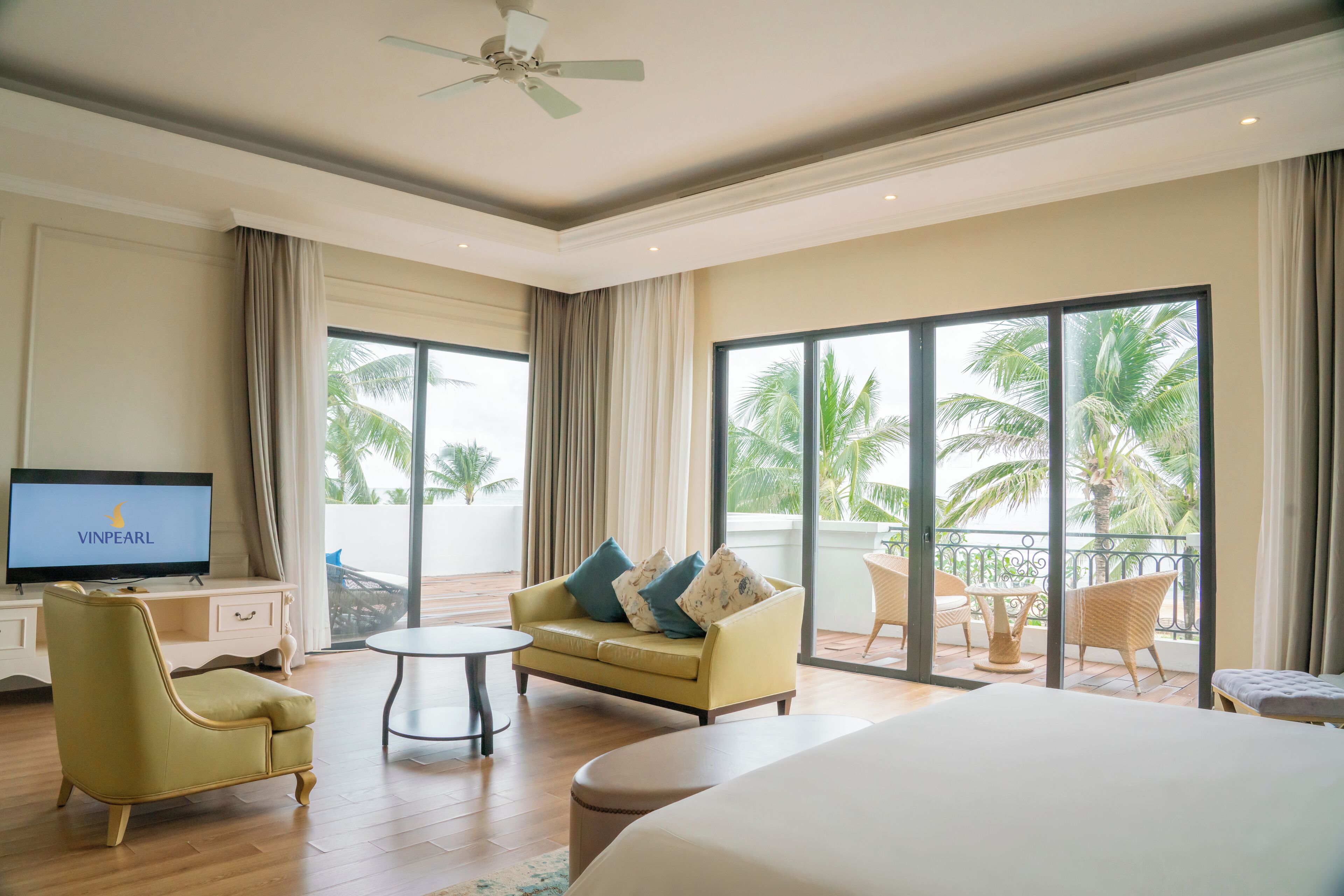 A hotel room with a bed, a sofa, a television, and a balcony with outdoor furniture.