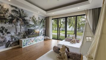 Amplia sala de estar con un gran mural de plantas tropicales, un televisor de pantalla plana y una zona de estar acogedora con cojines y un perro de peluche.